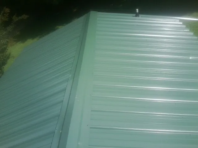 New green metal panels meeting at the ridge of a roof — Flat Roof Repair work by our crew in Junction City